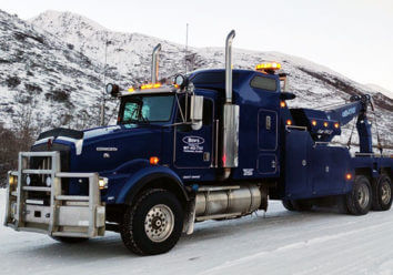 Ben's Towing truck towing large rig down snowy highway.